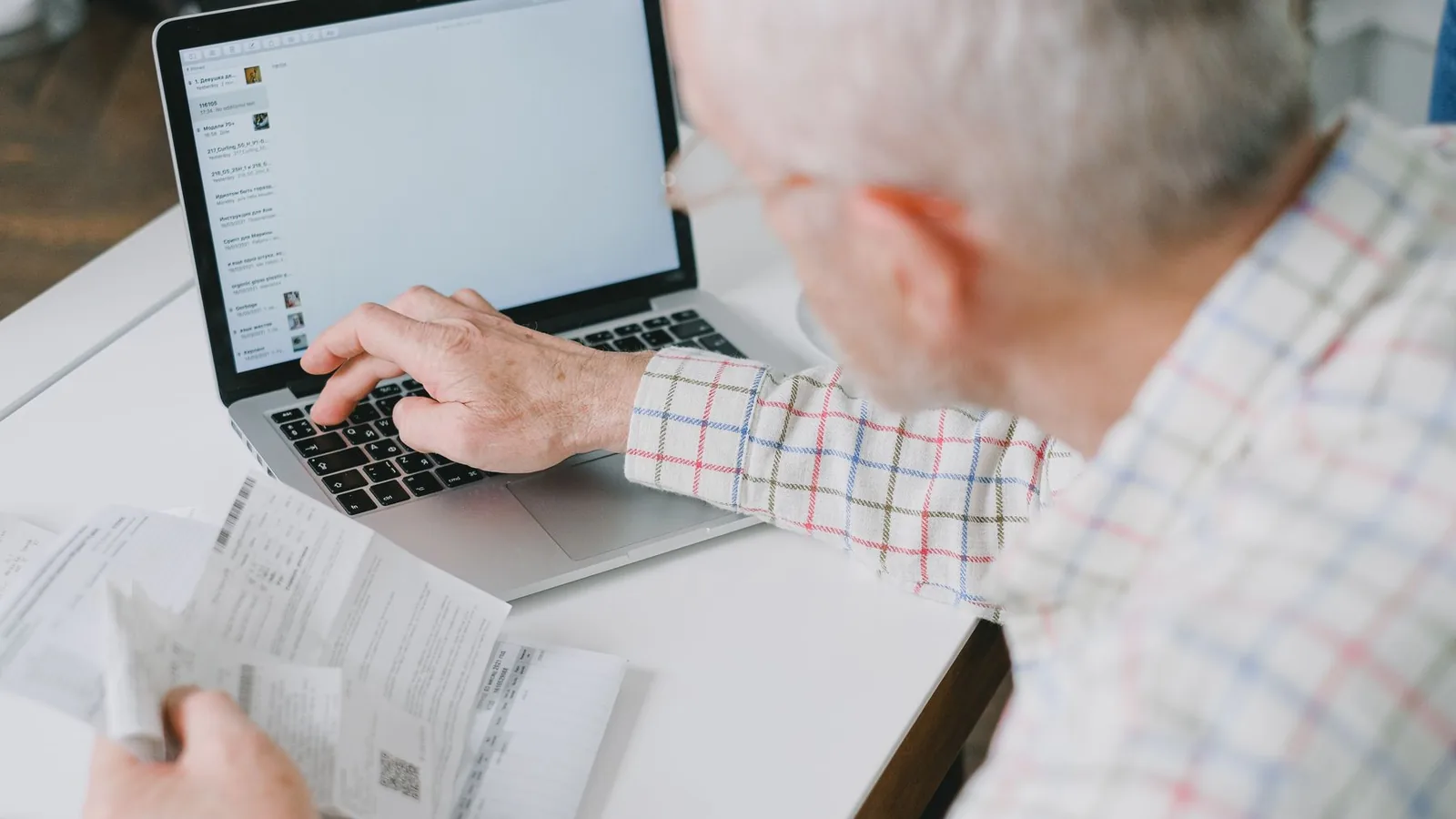 Homem mais velho revisando documentos ao lado de um laptop