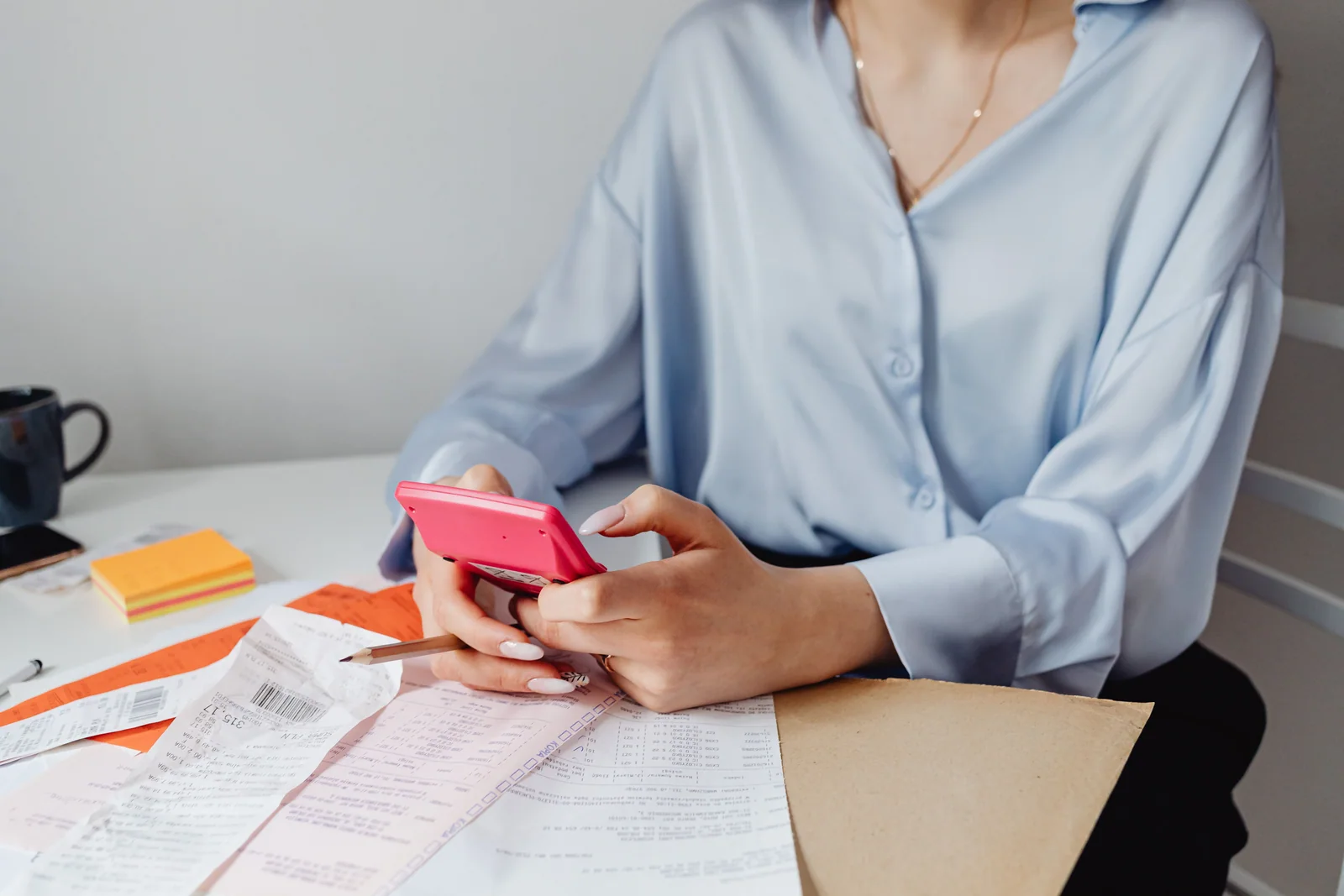 Pessoa conferindo despesas e recibos com uma calculadora no celular