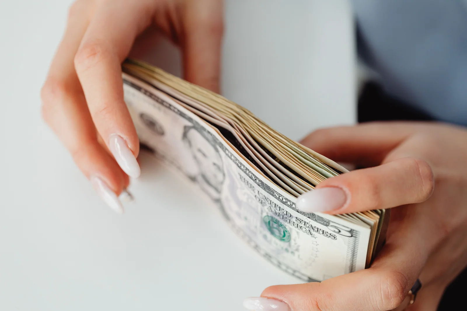 Duas mãos abrindo um leque de notas de dólar sobre uma mesa clara, antes de saber se o cheque foi pago