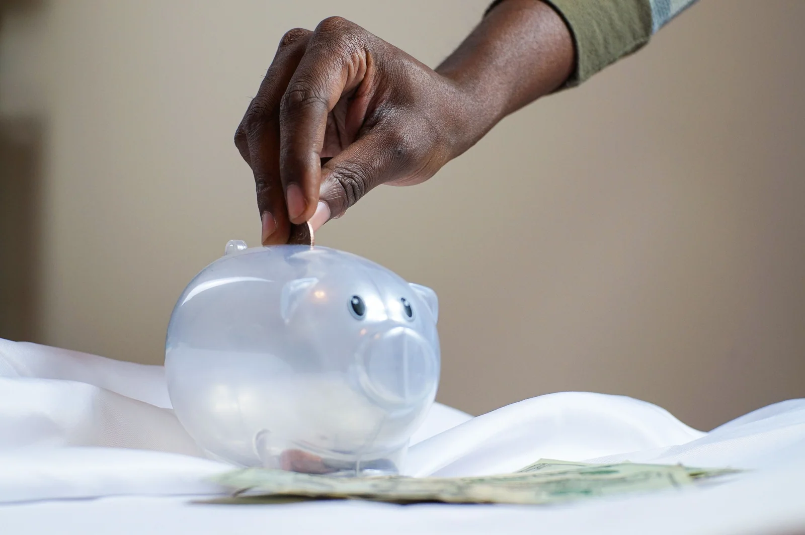 Mão colocando uma moeda em um cofre transparente ao lado de dólares