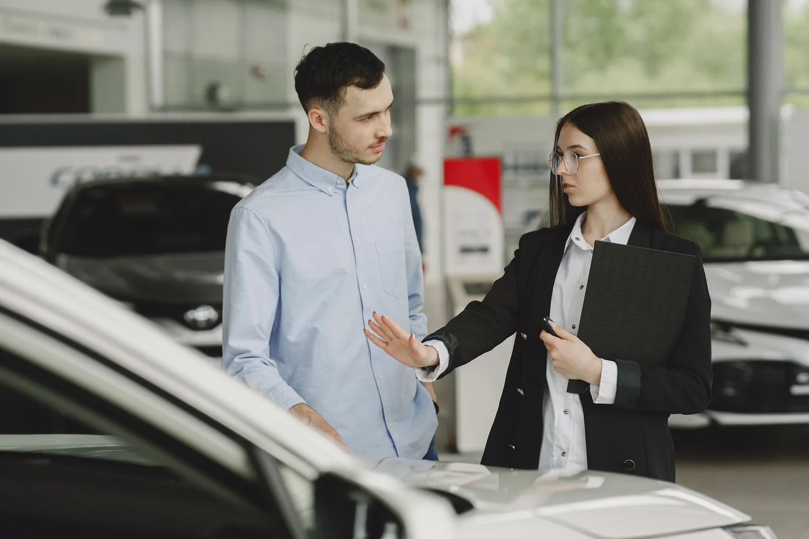 Cliente e vendedora conversando ao lado de um carro no showroom