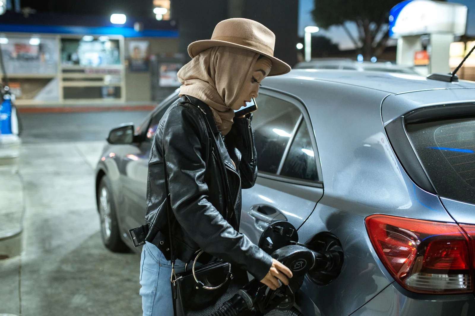 Mulher ao telefone abastecendo um carro cinza em um posto à noite