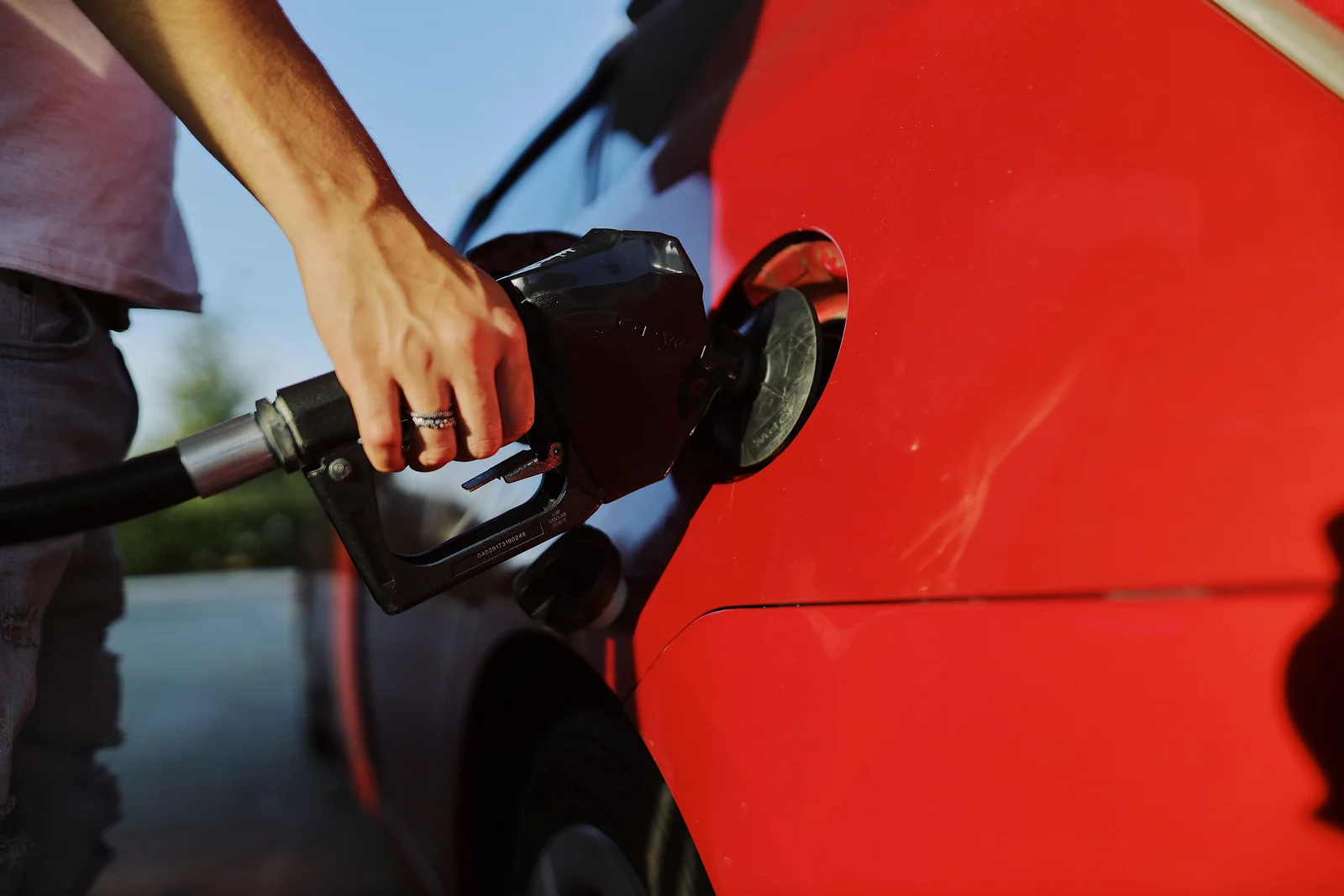 Pessoa abastecendo um carro vermelho em um posto, com a bomba no tanque