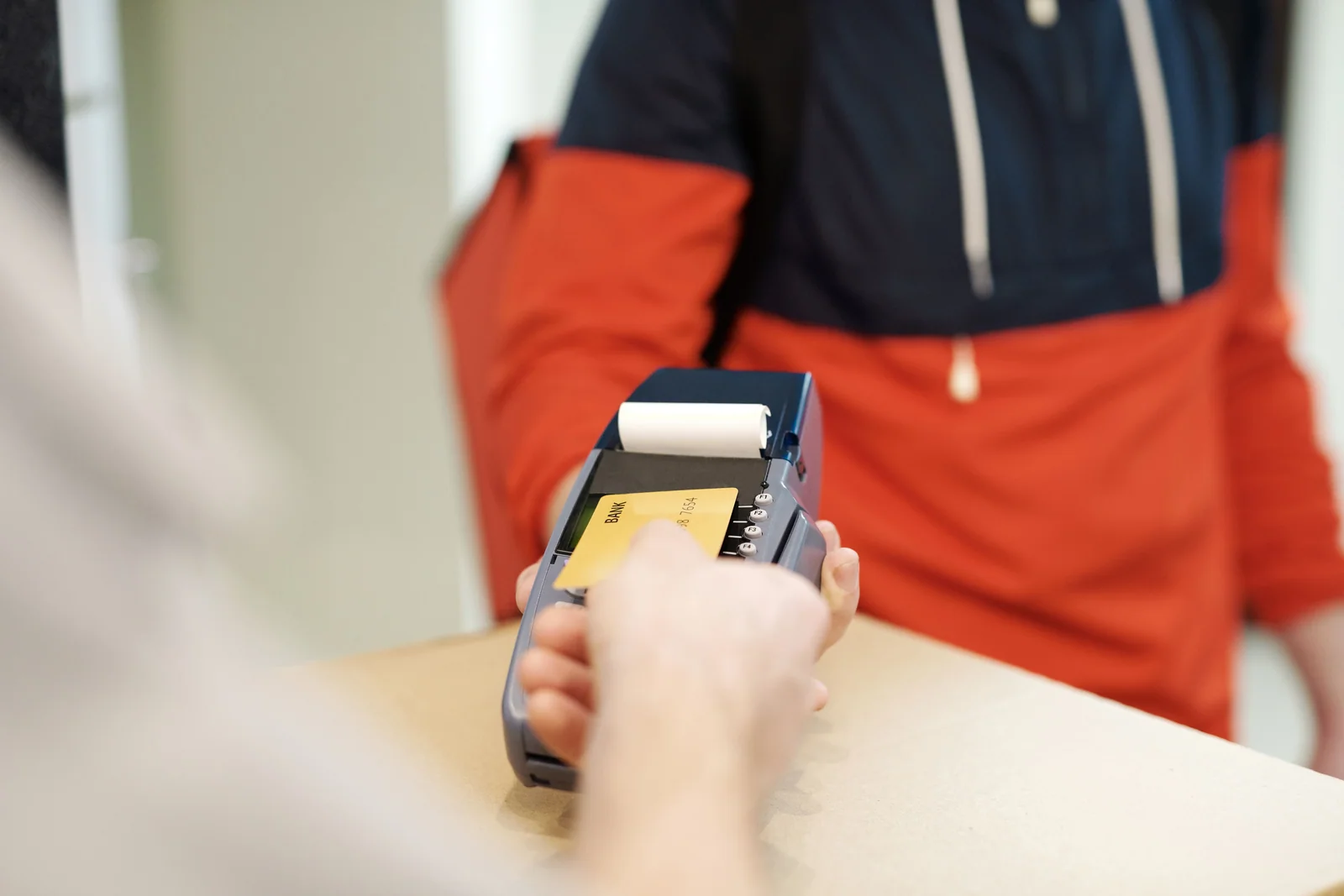 Mão aproximando um cartão de crédito de uma maquininha de pagamento