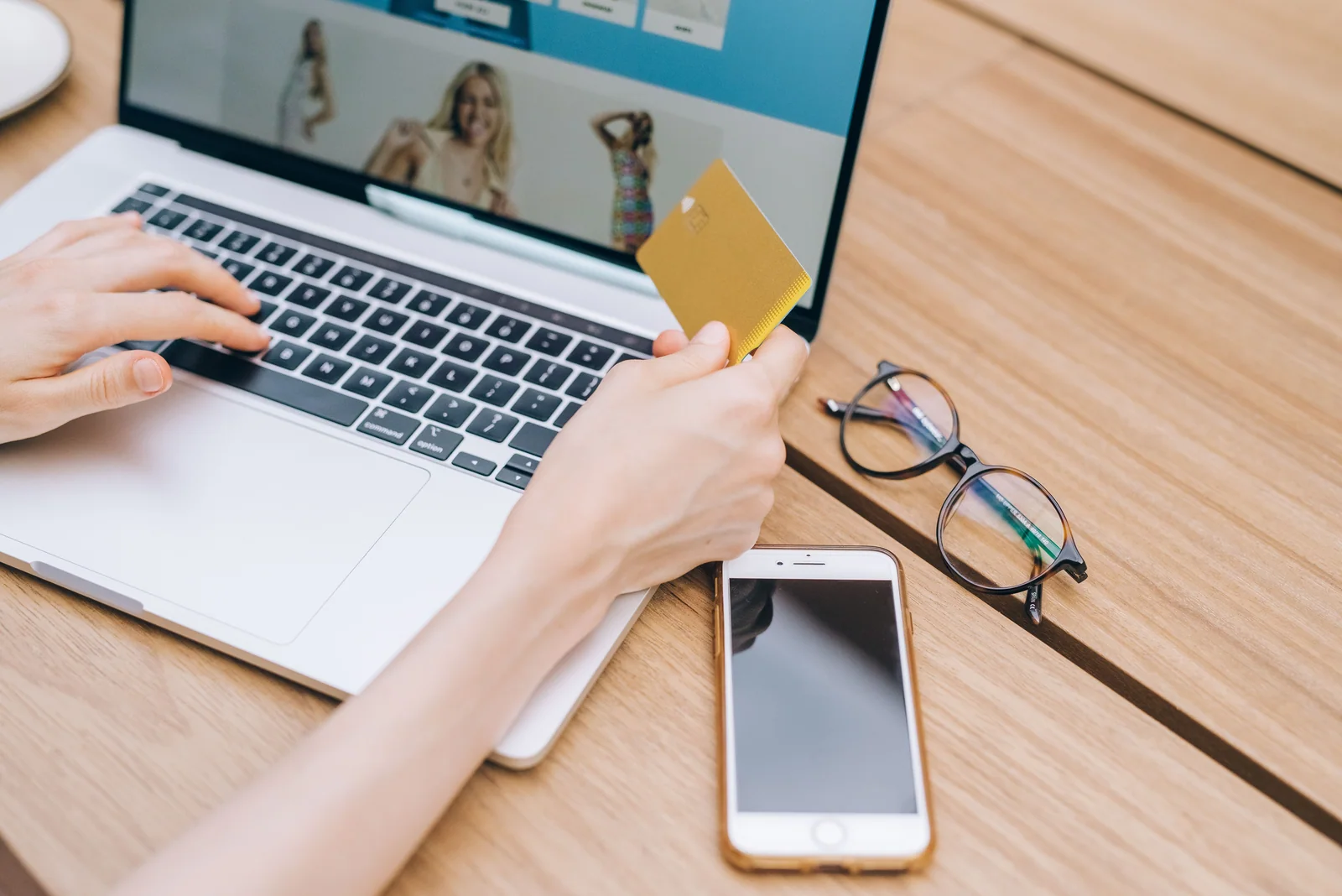 Pessoa usando cartão, laptop e celular em uma compra online