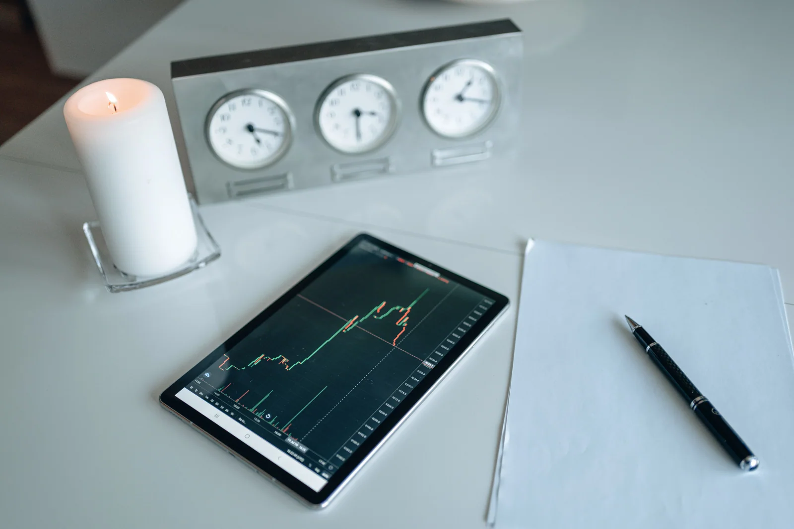 Tablet com gráfico de mercado ao lado de papel, caneta e relógio de mesa