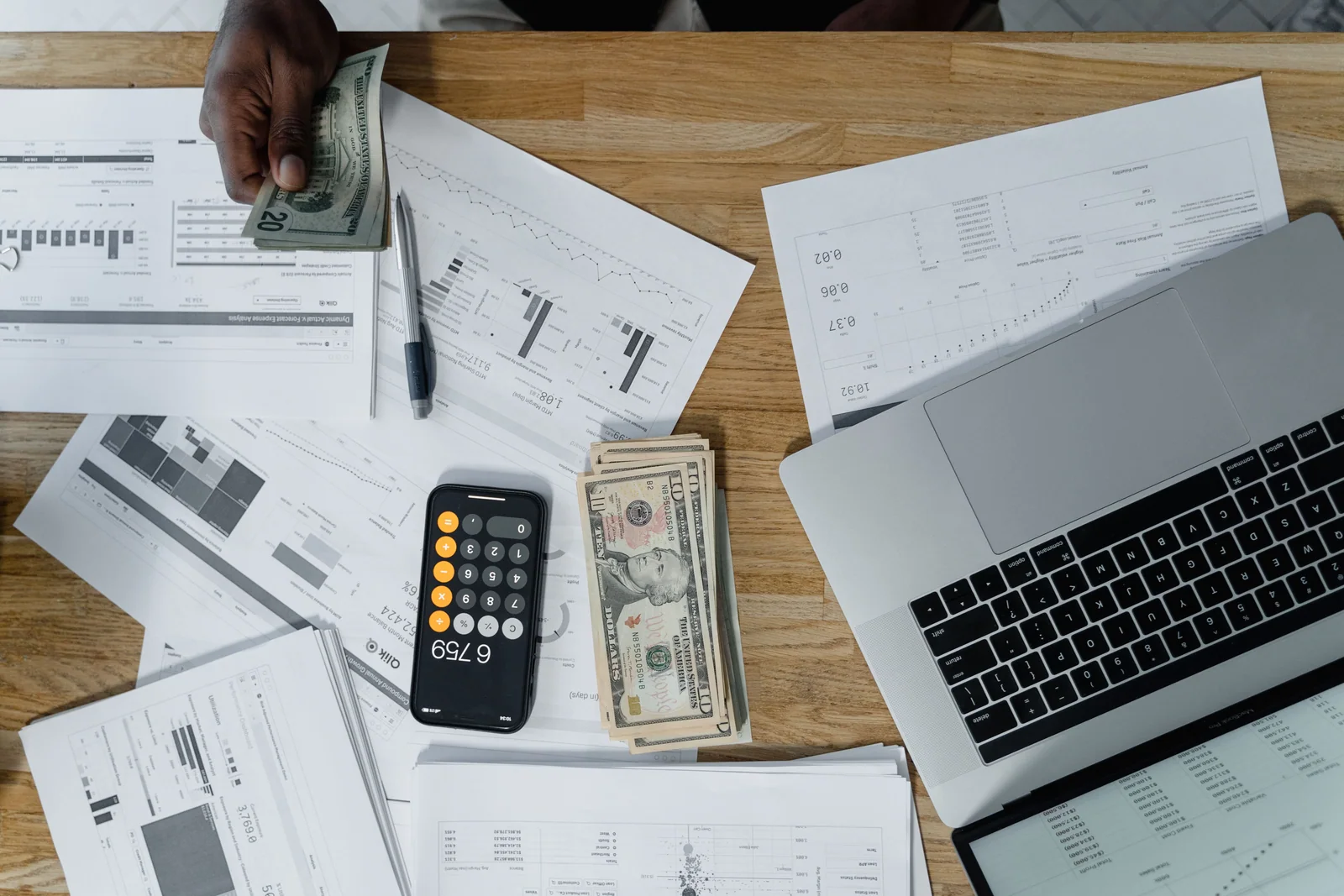 Mesa com laptop, calculadora, dinheiro e documentos usados para planejar investimentos